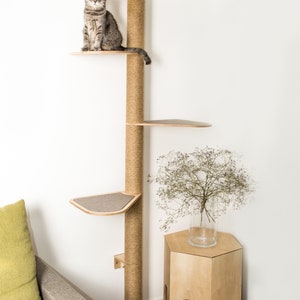 Puede incluir: Un gato se sienta en un &aacute;rbol para gatos de madera con un poste para rascar de cuerda de sisal. El &aacute;rbol para gatos tiene varias plataformas y est&aacute; montado en una pared. Una peque&ntilde;a mesa de madera con un agujero est&aacute; en la esquina.