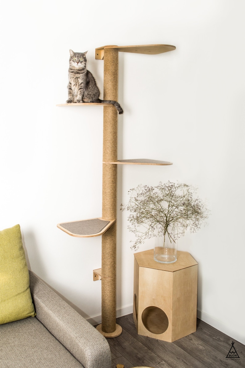 Puede incluir: Un gato se sienta en un &aacute;rbol para gatos de madera con un poste para rascar de cuerda de sisal. El &aacute;rbol para gatos tiene varias plataformas y est&aacute; montado en una pared. Una peque&ntilde;a mesa de madera con un agujero est&aacute; en la esquina.