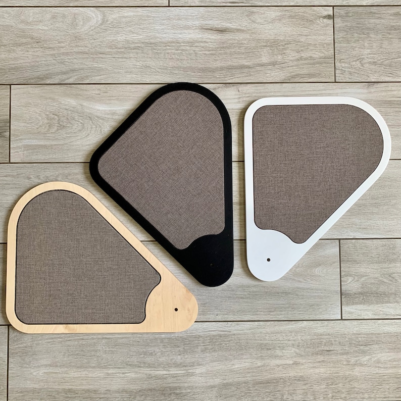 May include: Three cat scratching posts shaped like triangles. The posts are made of wood and covered in a brown fabric. The posts are in different colours: black, white, and natural wood.
