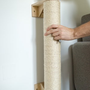 Pu&ograve; includere: Un tiragraffi rivestito in corda beige montato su una staffa da parete in legno. Il palo &egrave; in fase di installazione con un cacciavite.