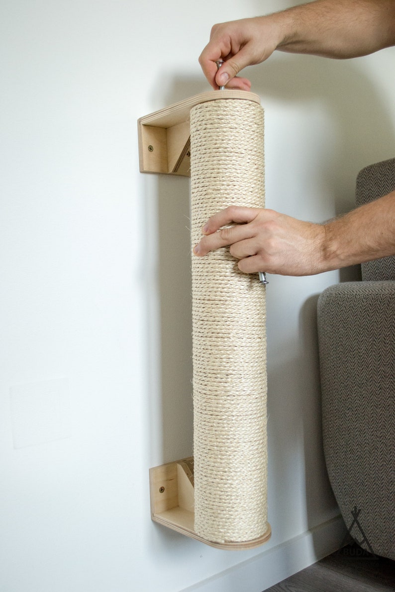 Pu&ograve; includere: Un tiragraffi rivestito in corda beige montato su una staffa da parete in legno. Il palo &egrave; in fase di installazione con un cacciavite.
