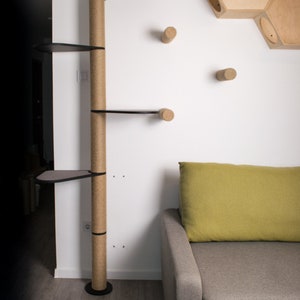 Puede incluir: Un &aacute;rbol para gatos alto con un poste cubierto de sisal y m&uacute;ltiples plataformas. El &aacute;rbol est&aacute; hecho de madera y tiene una plataforma superior negra. El &aacute;rbol est&aacute; en una habitaci&oacute;n con un sof&aacute; y un juguete para gatos montado en la pared.
