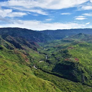 May include: A panoramic view of a lush green valley with a winding river running through it. The valley is surrounded by steep, rocky hillsides. The sky is blue with white clouds.