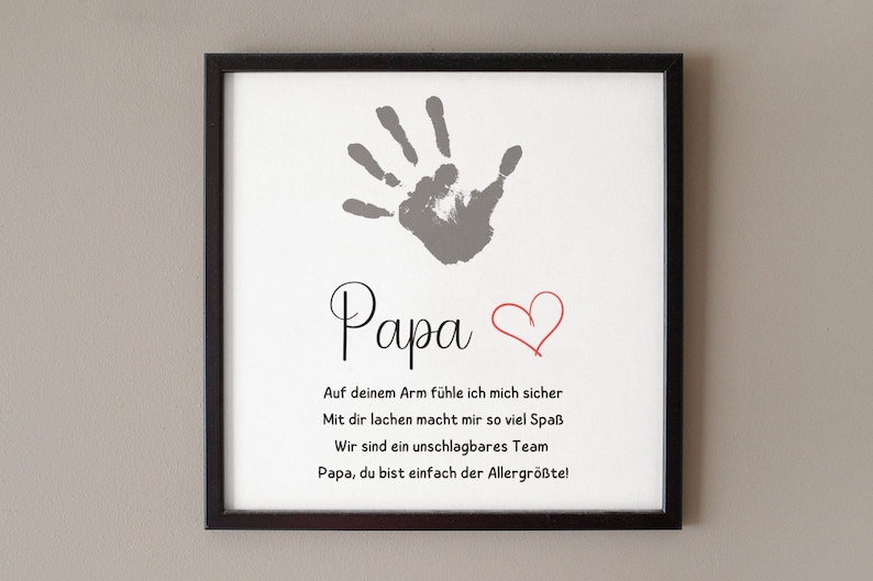 May include: Framed print with a black border featuring a gray handprint, the word "Papa" in script, and a red heart. Below, German text expresses affection. A heartfelt gift for Father's Day or a special occasion.