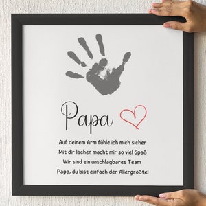 May include: A framed print with a handprint and the word "Papa" in script. Below, text in German reads, "On your arm I feel safe..." A red heart is drawn next to the word "Papa".