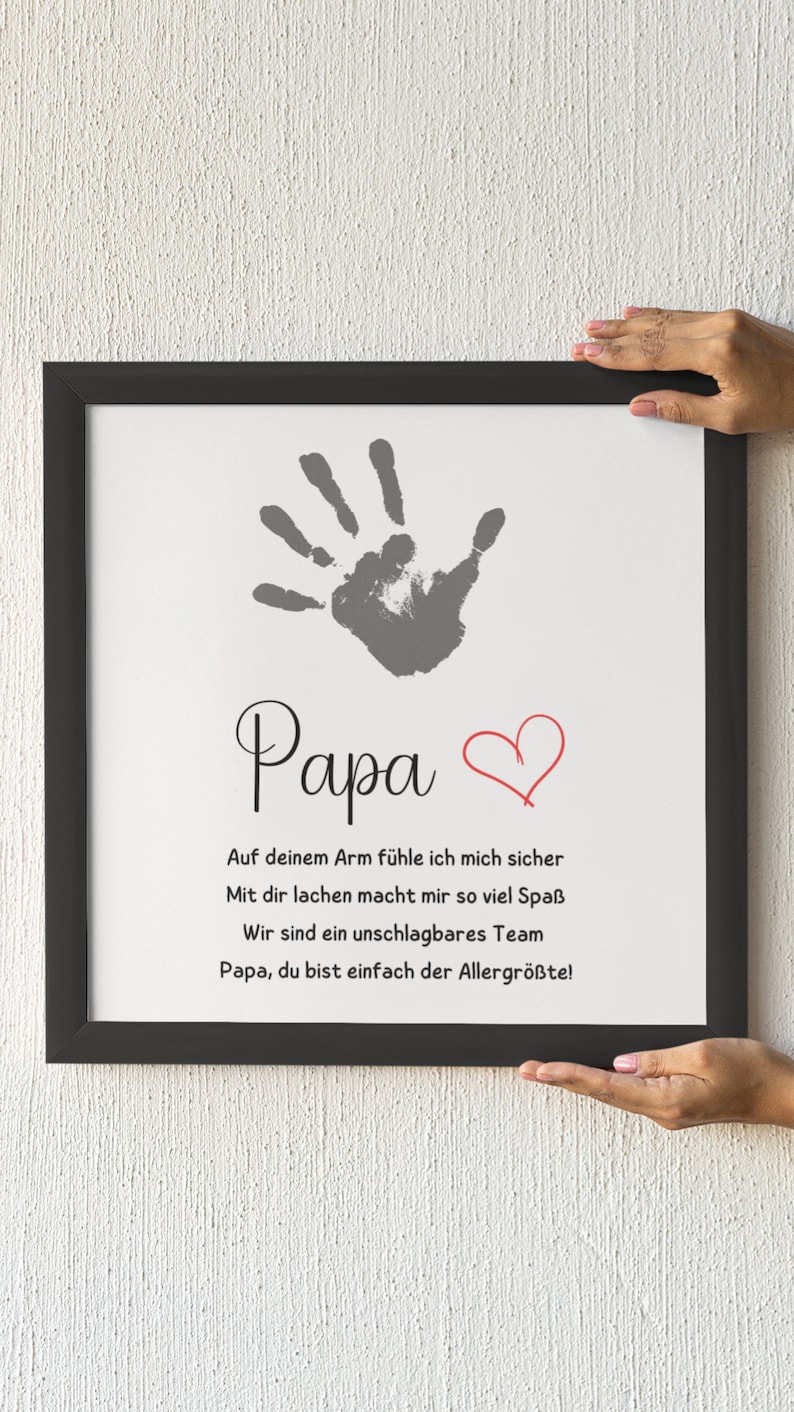 May include: A framed print with a handprint and the word "Papa" in script. Below, text in German reads, "On your arm I feel safe..." A red heart is drawn next to the word "Papa".