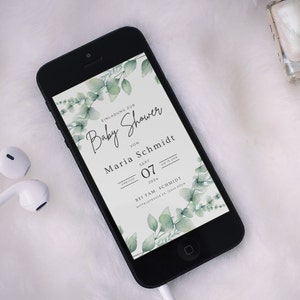 May include: A black smartphone displays a baby shower invitation. The invitation features elegant script and botanical accents. The text includes the words "Baby Shower", the name "Maria Schmidt", and the date "Sept 07, 2024". Green eucalyptus leaves frame the text.