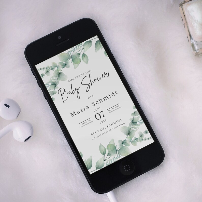 May include: A black smartphone displays a baby shower invitation. The invitation features elegant script and botanical accents. The text includes the words "Baby Shower", the name "Maria Schmidt", and the date "Sept 07, 2024". Green eucalyptus leaves frame the text.
