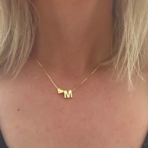 May include: A gold necklace with a heart charm and a letter 'M' charm.