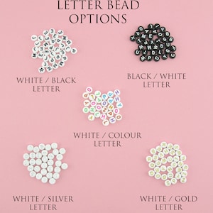 May include: Four different color combinations of letter beads. White beads with black letters, white beads with colorful letters, white beads with silver letters, and white beads with gold letters.