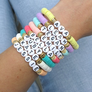 May include: A stack of colourful beaded bracelets with white letter beads spelling out the names Ava, Leah,  Gan,  Emily, Bella, Ruby, Kate, Jessie, and  Jack.