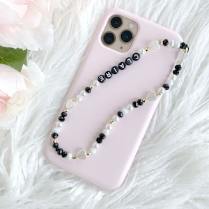 May include: A pink phone case with a black and white beaded phone strap with the word "CLAIRE" spelled out in black beads.