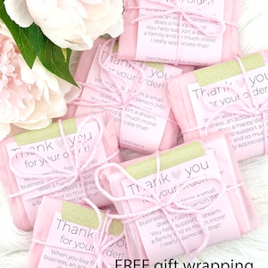 May include: Four pink gift boxes with gold glitter accents and white string tied around them. Each box has a thank you note with the text "Thank you for your order!" and a message about supporting a small business. The boxes are on a white fluffy surface. Free gift wrapping for orders over $50.