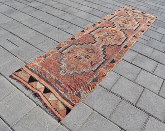 Könnte beinhalten: Ein langer, schmaler Teppich mit einem geometrischen Muster in Orange-, Braun- und Schwarztönen. Der Teppich liegt auf einer grauen Betonfläche.