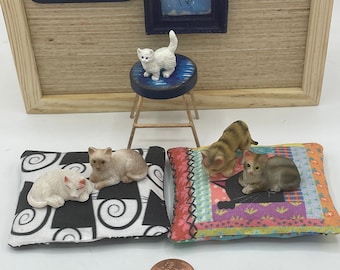 Könnte beinhalten: Vier weiße, braune und getigerte Katzen im Miniaturformat auf bunten Stoffkissen. Eine weiße Katze sitzt auf einem blauen und goldenen Hocker. Eine Cent-Münze befindet sich im Vordergrund zur Größenbestimmung.