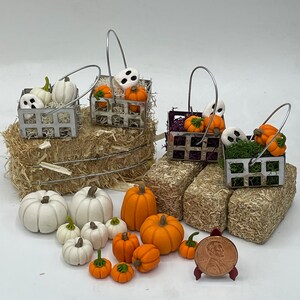 以下が含まれることがあります： ミニチュアのハロウィーンと秋の装飾のセット。白いカボチャと幽霊でいっぱいのワイヤーバスケットが3つと、小さな白とオレンジのカボチャのセットが含まれています。装飾はわらの上に置かれています。