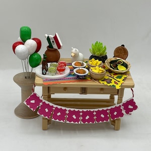 May include: A miniature wooden table set with a festive Mexican theme. The table is decorated with a colorful tablecloth, a string of pink paper flags, and a variety of miniature food items, including guacamole, chips, and drinks. There are also miniature balloons, a small llama figurine, and a small Mexican flag.
