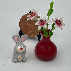 May include: Miniature gray bunny figurine with pink-lined ears and a red nose. A small red vase holds delicate white and pink flowers. A penny is used to show the scale of the tiny objects.
