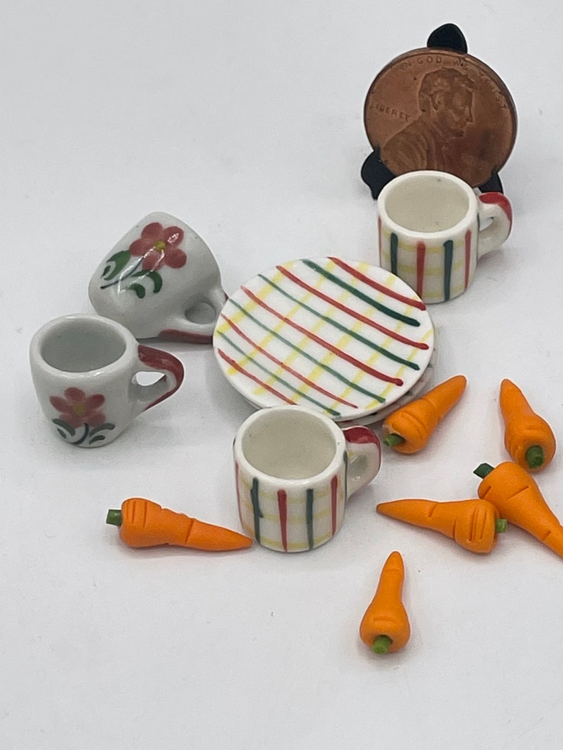 May include: Miniature ceramic tea set with two floral-decorated cups, two striped cups, a striped plate, and several orange carrot miniatures. A penny is included for scale. Perfect for dollhouses or craft projects.