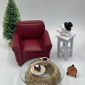 May include: A miniature living room scene with a red armchair, a glass-top coffee table with a wicker base, a white end table with a small white bear wearing a top hat, a miniature Christmas tree, a slice of cake on a plate, and a mug of hot chocolate with a candy cane.