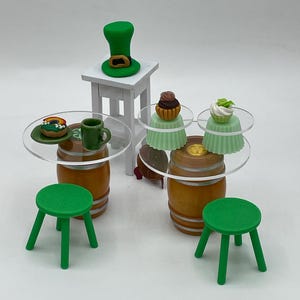 May include: Miniature St. Patrick's Day themed set with a green leprechaun hat, cupcakes, and stools. The set includes small wooden barrels, clear acrylic tabletops, and a white table. The cupcakes have green and brown frosting.