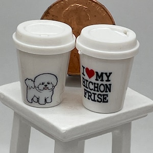 May include: Two white ceramic coffee mugs with a design. One mug has a cartoon image of a white Bichon Frise dog. The other mug has the text "I love my Bichon Frise" with a red heart.