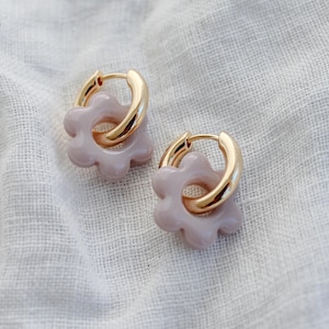 Könnte beinhalten: Ein Paar goldene Creolen mit einem hellrosa Blumenanhänger. Der Blumenanhänger ist aus Keramik und hat eine strukturierte Oberfläche.