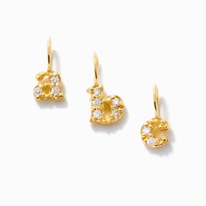 May include: Three gold-toned letter charms featuring the lowercase letters a, b, and c. Each charm is embellished with small, clear, sparkling stones set into the metal surface and includes a small loop at the top for attachment to a chain.