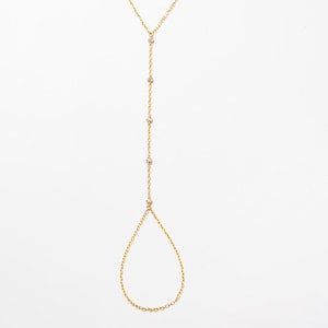 Puede incluir: Un brazalete de cadena dorada con un lazo en forma de lágrima y pequeñas piedras transparentes.