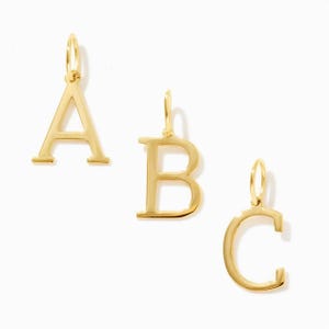 May include: Three gold-toned metal letter charms shaped as the letters A, B, and C. Each charm features a smooth, polished surface and includes a small circular jump ring at the top for attachment, presented in a clean, simple arrangement.