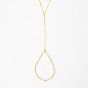 May include: A gold-toned metal chain hand harness featuring a delicate cable chain design. The jewelry piece consists of a vertical chain segment that connects to a teardrop-shaped loop, designed to be worn around the finger and wrist area.