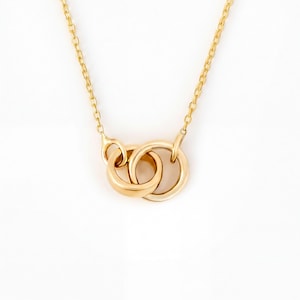 May include: A gold-toned necklace featuring a delicate chain and a pendant composed of two interlocking circular rings. The metal has a polished, reflective finish, and the design showcases a simple, continuous loop structure suspended from the chain.
