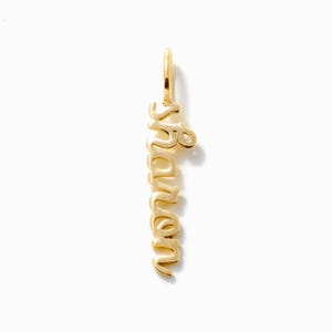May include: A vertical gold pendant featuring the name Sharon written in a continuous, flowing cursive script. The metal has a polished, reflective finish, and a small circular jump ring is attached to the top for hanging on a chain or cord.