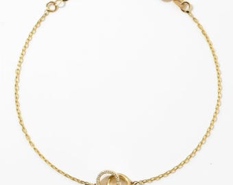May include: A gold chain bracelet featuring two interlocking circular charms. One circle is plain polished gold, while the other is encrusted with small clear stones. The bracelet includes a delicate chain with a spring ring clasp and an extender.