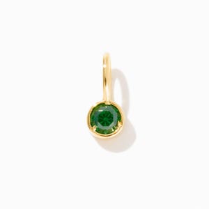 May include: A gold charm with a green gemstone. The charm is round and has a simple design.