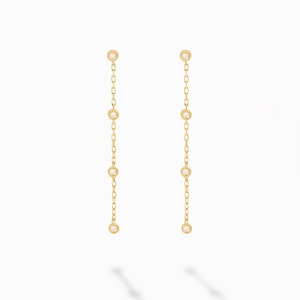 Puede incluir: Un par de pendientes de oro con un delicado diseño de cadena y pequeñas piedras transparentes.