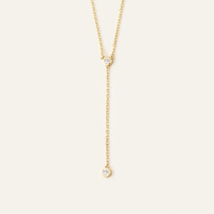 May include: A delicate gold chain necklace with two small round diamonds. The necklace is a Y-shape with a diamond at the top and bottom of the Y.