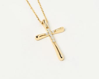 Può includere: Una collana in oro con un ciondolo a croce dalla finitura lucida. Il centro della croce è impreziosito da una fila verticale di cinque piccole pietre trasparenti a taglio rotondo. Il ciondolo pende da una sottile catena a maglie dorate.