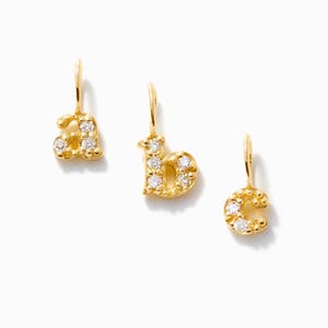 May include: Three gold-toned letter charms, specifically the lowercase letters a, b, and c. Each charm features a textured surface and is embellished with small, clear, round-cut stones set into the metal, complete with a small loop at the top.
