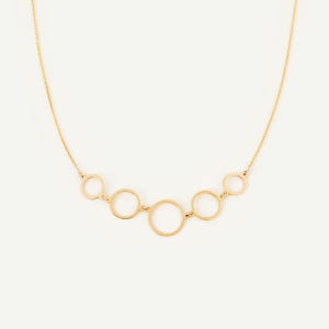 May include: A gold-toned necklace featuring a delicate chain and a central focal point composed of five interconnected circular rings of varying sizes, arranged in a symmetrical arc pattern that hangs horizontally across the center.