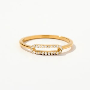May include: A gold ring featuring a rectangular centrepiece adorned with small, clear gemstones. The slender band is polished, and the ring is set against a white backdrop. This is a piece of jewellery.