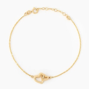 May include: A delicate gold chain bracelet featuring two interlocking heart-shaped charms at the center. The bracelet is constructed with fine, polished gold links and includes a small circular clasp mechanism at the top for secure fastening.