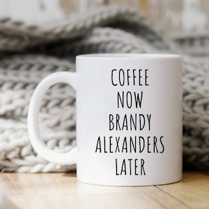May include: White ceramic coffee mug with black text that reads "Coffee Now Brandy Alexanders Later".