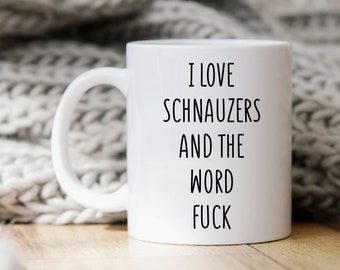 May include: White ceramic mug with the text "I LOVE SCHNAUZERS AND THE WORD FUCK" in black. The mug has a white handle and is set against a neutral background.