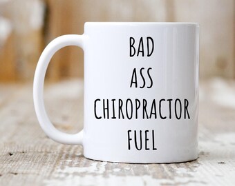 May include: White ceramic coffee mug with black text that reads "Bad Ass Chiropractor Fuel".