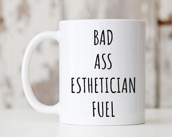 Könnte beinhalten: Weiße Keramik-Kaffeetasse mit schwarzem Text, der "Bad Ass Esthetician Fuel" lautet.