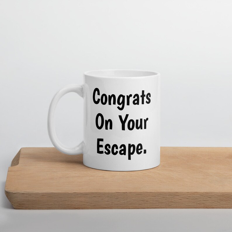 May include: White ceramic coffee mug with black text that reads "Congrats On Your Escape."
