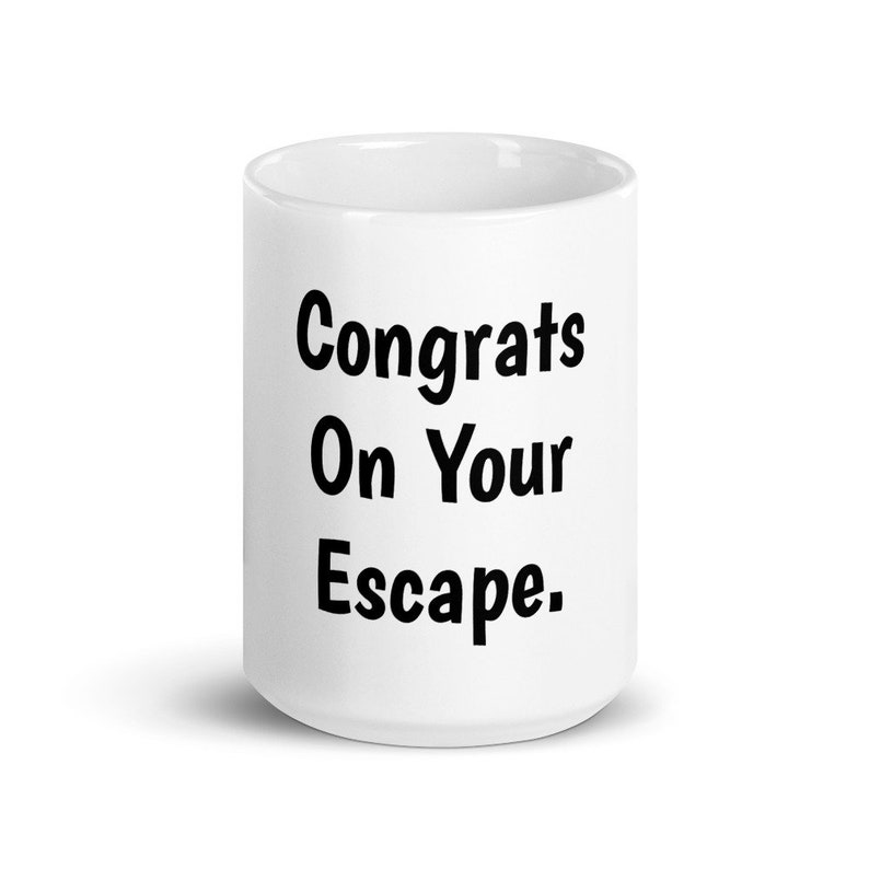 May include: White ceramic coffee mug with black text that reads "Congrats On Your Escape."
