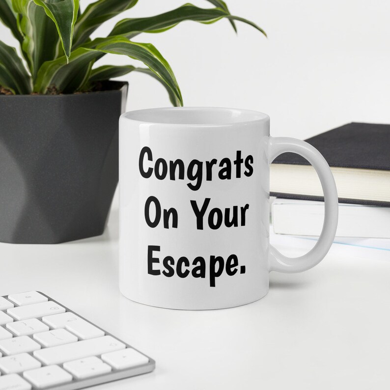 May include: White ceramic coffee mug with black text that reads "Congrats On Your Escape."