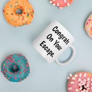 May include: White ceramic mug with black text that reads "Congrats On Your Escape."